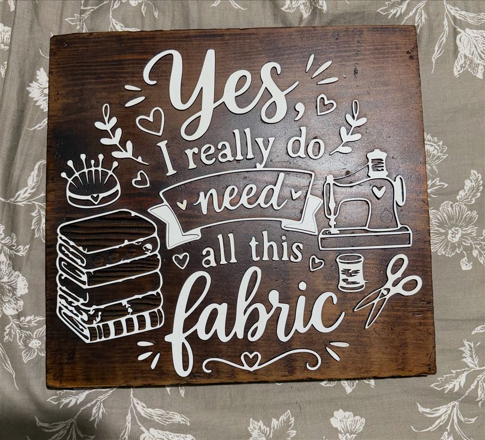 Walnut stained sign reading Yes, I really do need all this fabric, with cream cut lettering and sewing icons