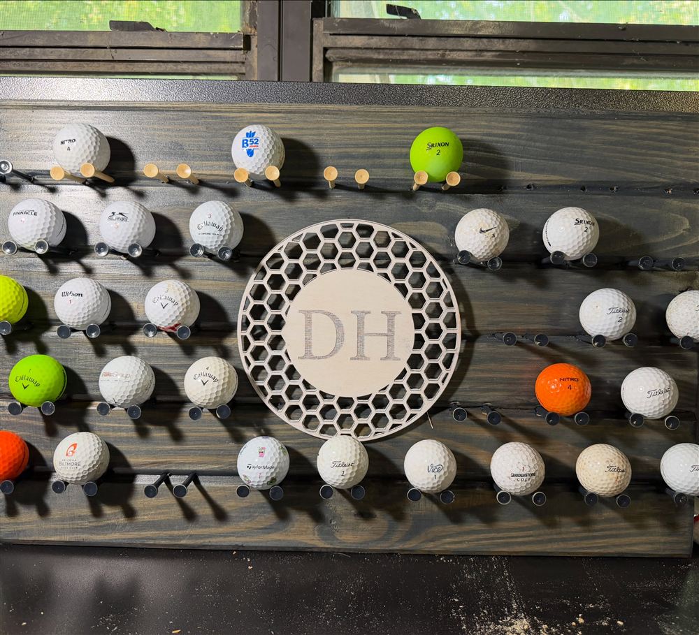 Dark stained golf ball display board with rows of pegs and a cut DH monogram in the center