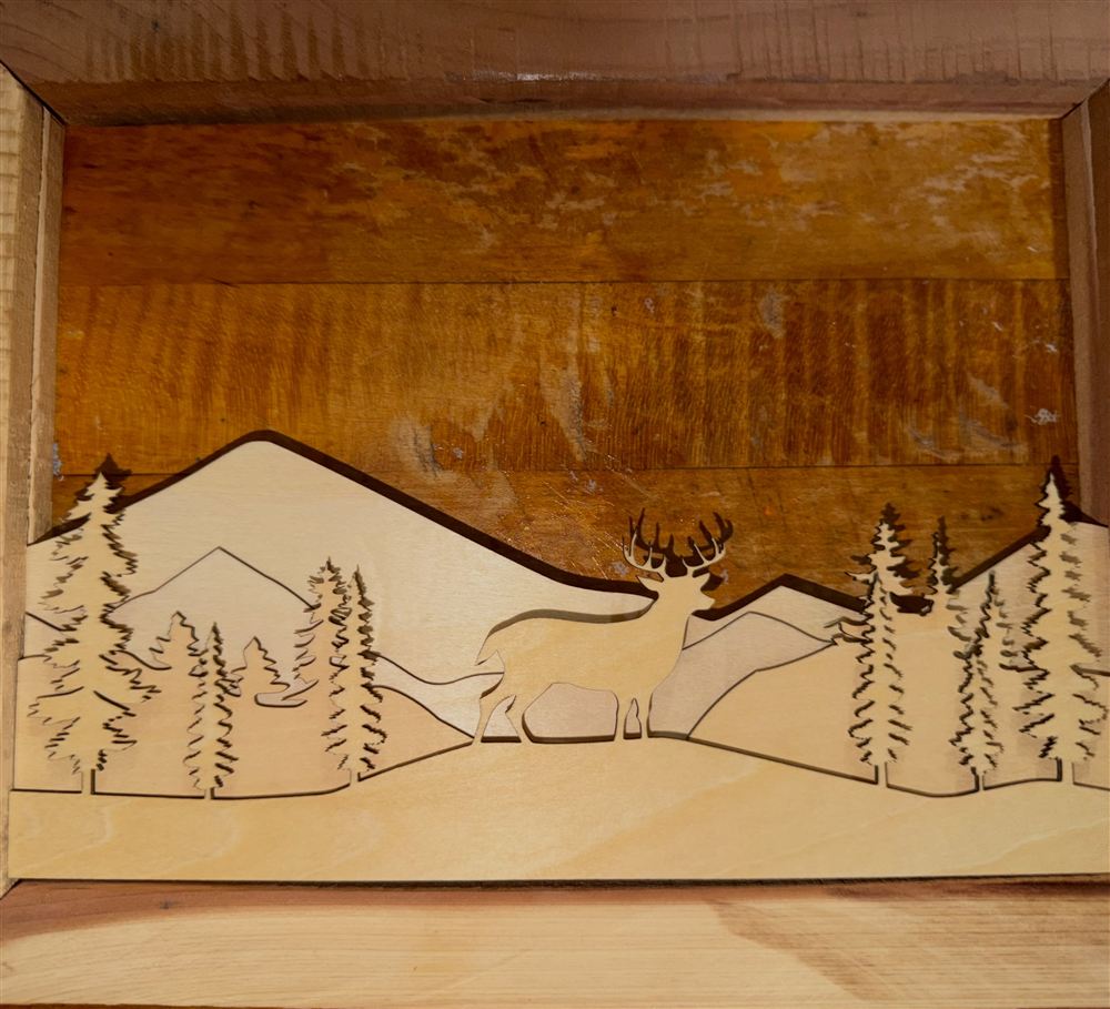 Layered birch cutout of mountains, pines and a deer in a reclaimed wood shadow box