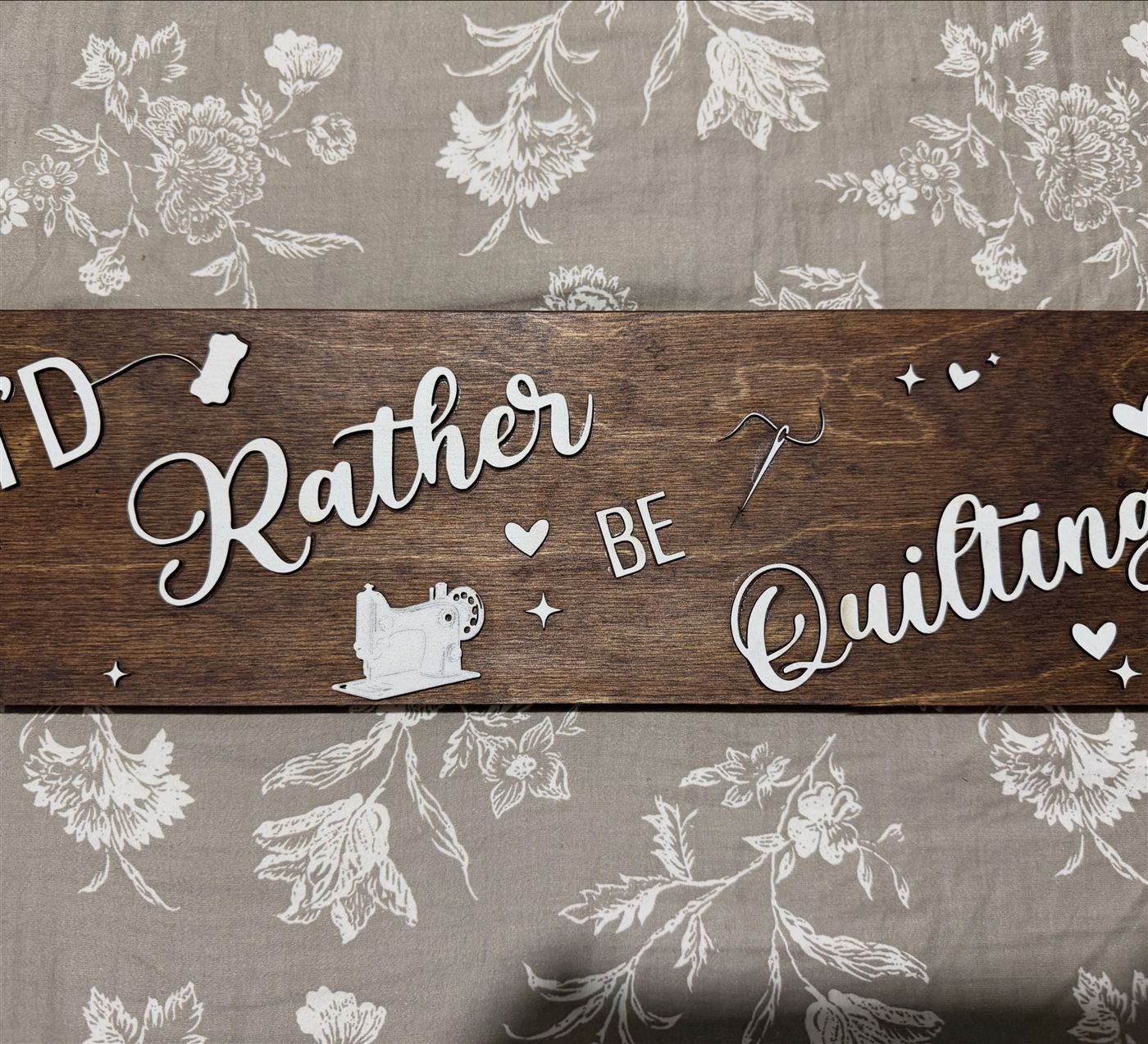 Long walnut stained sign reading I'd Rather Be Quilting with cream script letters